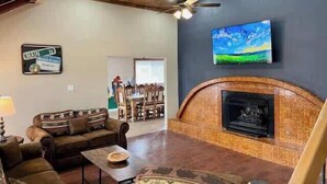 A living room with a fireplace, a television mounted on the wall, and a dining area in the background.