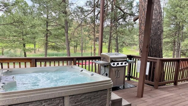 A hot tub on a wooden deck with a grill and a stone facade.