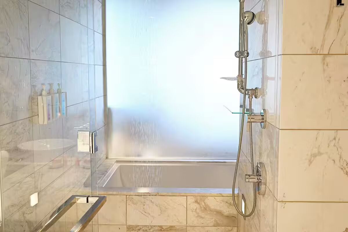 A modern bathroom with a glass-enclosed shower, a marble-tiled floor, and a glass shower door.