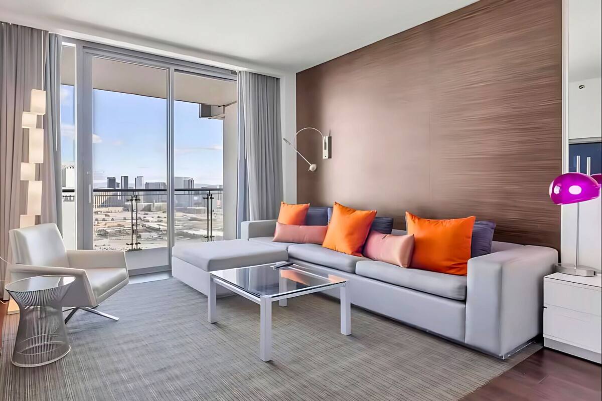A modern hotel room with a large sliding glass door leading to a balcony with a city view.