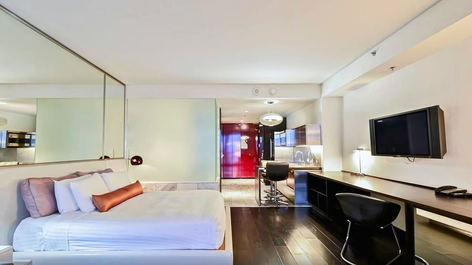 A modern hotel room with a large bed, a desk with a chair, a TV, and a mirror.