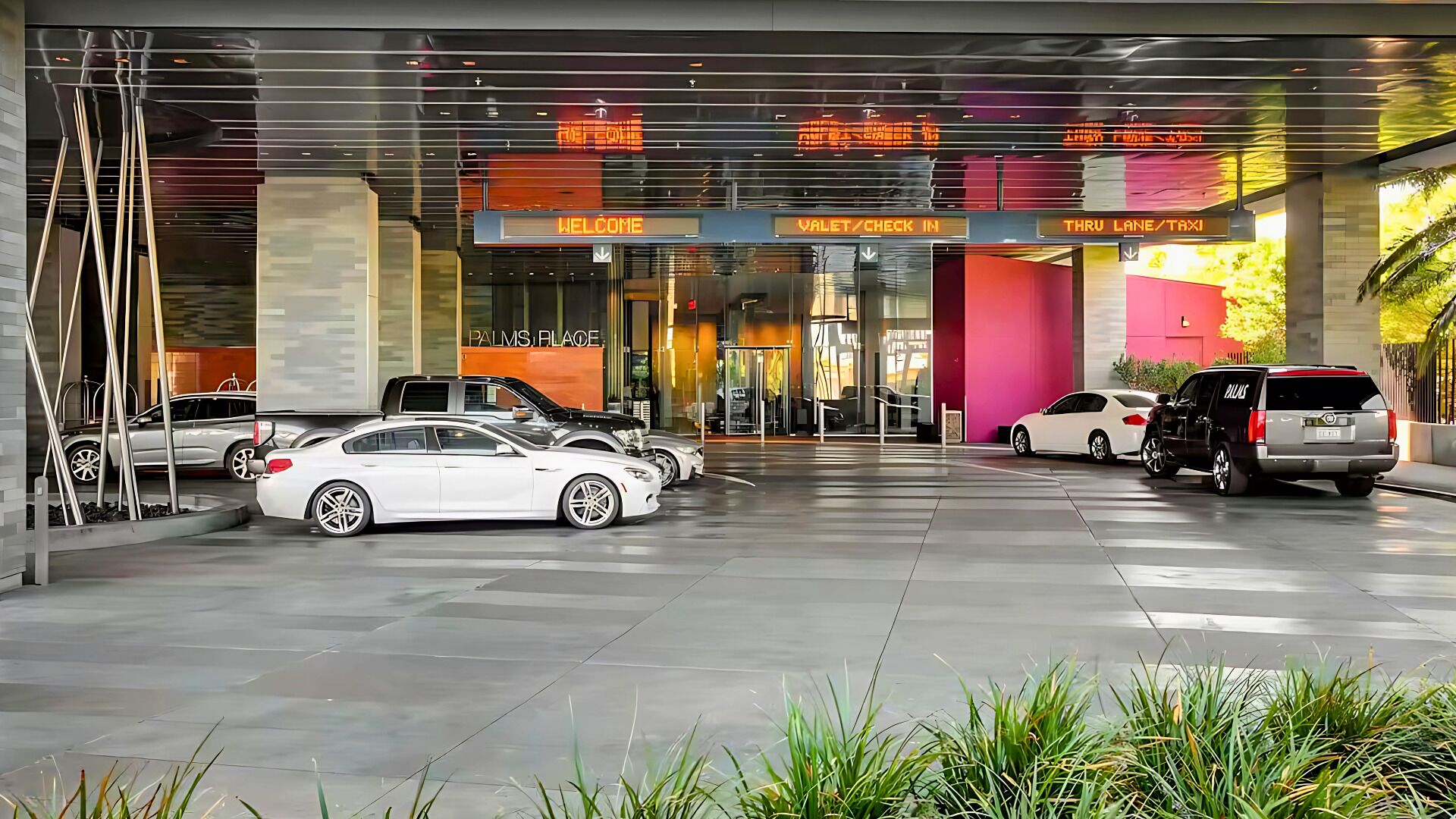A modern hotel entrance with a glass facade, multiple parking spaces, and directional signage for valet, check-in, and taxi services.