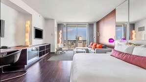 Una camera d'hotel moderna con un letto grande, una scrivania, un divano e un balcone con vista sulla città.