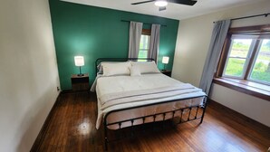 Ein Schlafzimmer mit einem Metallbettgestell, zwei Nachttischen mit Lampen, einem fenster mit Vorhängen und einem Deckenventilator.