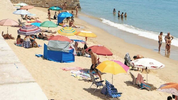 Une plage avec des murets en pierre, des parasols et des gens.