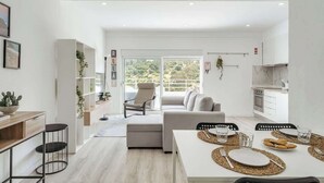 Un espace de vie moderne et décloisonné, comprenant un coin repas, une cuisine et un balcon offrant une vue sur la verdure.