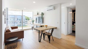 Un salon moderne avec un canapé, une table à manger et des chaises. Un téléviseur est fixé au mur et une plante est posée sur une étagère.