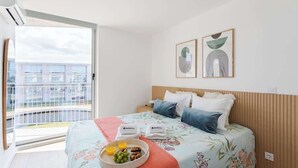 Une chambre à coucher avec un lit, des oreillers, une table de chevet, un panier de fruits et des œuvres d’art accrochées au mur.