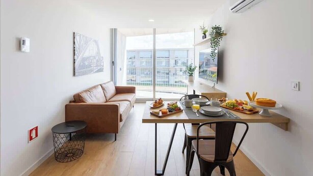 Un appartement moderne doté d’un coin repas, d’un canapé et d’une grande fenêtre donnant sur la ville.