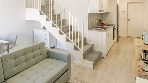 A modern apartment with a staircase leading to an upper level, a kitchen with a sink and a fruit bowl, and a living area with a sofa and a coffee table. - Charming Mezzanine Studio by HostWise (Porto)
