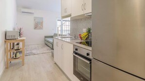 A modern kitchen with stainless steel appliances, a wooden side table with a kettle, and a fruit bowl on the counter. - Charming Mezzanine Studio by HostWise (Porto)