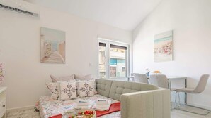 A modern bedroom with a bed, a sofa, a desk, and a chair. There are paintings on the walls and a window with a view. - Charming Mezzanine Studio by HostWise (Porto)
