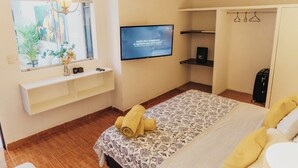 Hotellihuone, jossa on sänky, seinälle asennettu televisio, ikkuna, josta on näkymä vehreään maisemaan, ja vaatekaappi henkareineen.