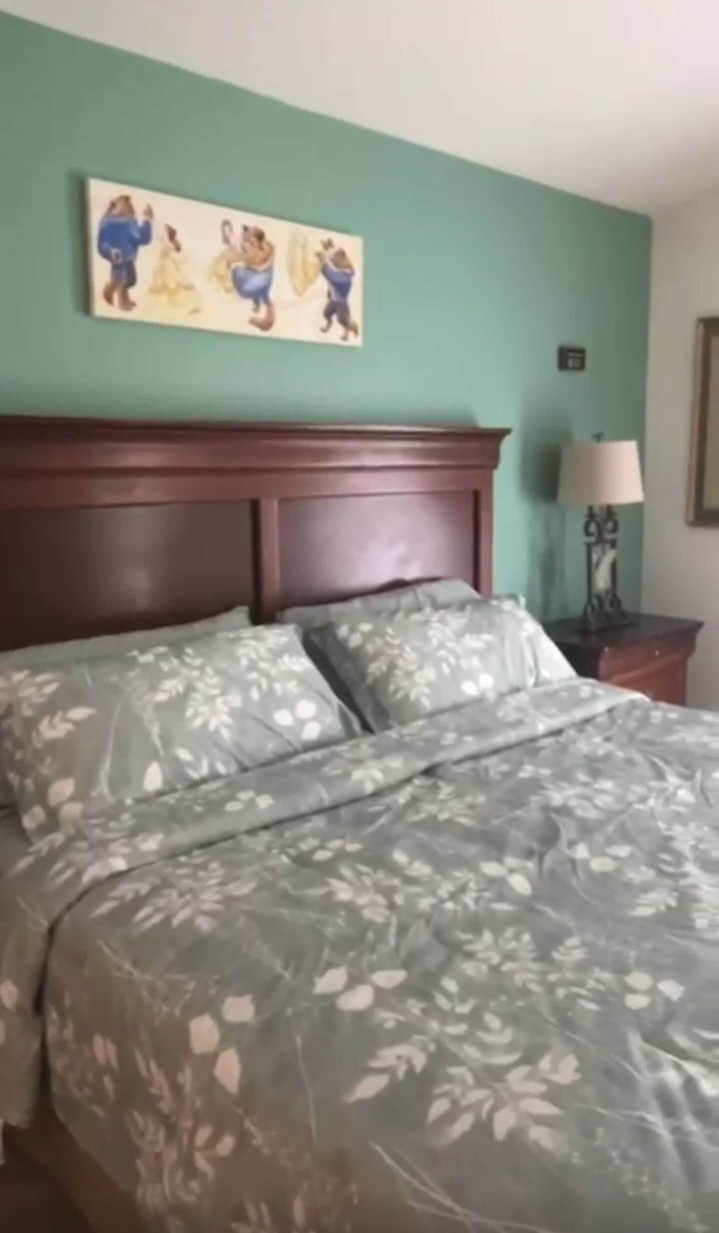 A bed with floral bedding, a wooden headboard, and a painting above it.