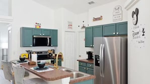 A modern kitchen with teal cabinets, stainless steel appliances, and Disney-themed decor.
