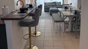 A modern kitchen with a bar area, dining space, and a living area with a sofa and curtains.
