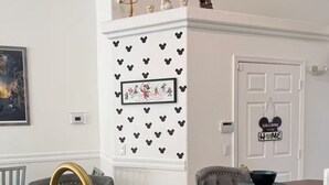 A kitchen with a stainless steel sink, a gold faucet, a white door with a 'Welcome to Our Home' sign, and a wall decorated with Mickey Mouse silhouettes.