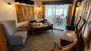 Una habitación acogedora con un sillón a cuadros, un sofá, una mesa de comedor con sillas y un ventilador de techo.