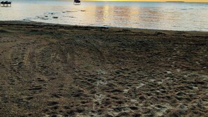 Una playa con huellas que conducen al agua, un bote y un atardecer lejano.