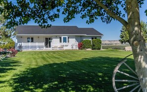 A two-story house with a front porch, a well-maintained lawn, and a clear view of the surrounding landscape. - Powell Farmstead Retreat- Dog Friendly, Comfortable Family Retreat (Powell)