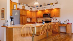 Une cuisine avec des meubles de rangement en bois, un îlot central doté de tabourets, un four à micro-ondes et une cuisinière.