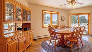 Un espace repas avec une table et des chaises en bois, un ventilateur de plafond et de grandes fenêtres.