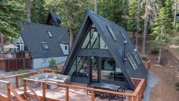 A modern house with a unique triangular roof, a deck with outdoor furniture, and a large glass door leading to an interior space.