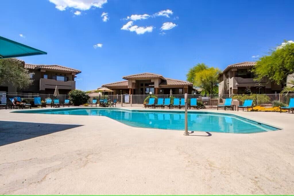 A pool area with blue lounge chairs and a clear blue sky.