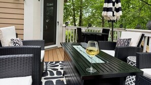 An outdoor patio with a black table and wicker chairs, a glass of white wine, and a striped umbrella. - EXQUISITE, DESIGNER HOME, 4BD/2.5BA, 4 miles from MAYO CLINIC (Rochester)