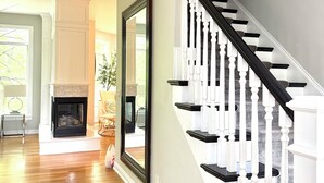 A staircase with black and white balusters, a fireplace, and a rug leading to a room with a large mirror. - EXQUISITE, DESIGNER HOME, 4BD/2.5BA, 4 miles from MAYO CLINIC (Rochester)