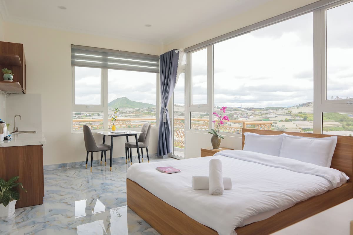 Habitación de hotel con cama, escritorio, silla, mesita, planta en maceta y vista a la ciudad.