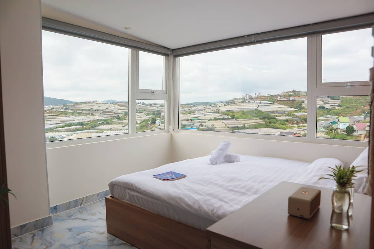 Una habitación de hotel con un ventanal que ofrece vistas a campos escalonados y edificios a la distancia.