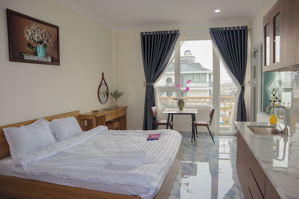 Habitación de hotel con cama, escritorio, ventana con cortinas, balcón y vistas a edificios.