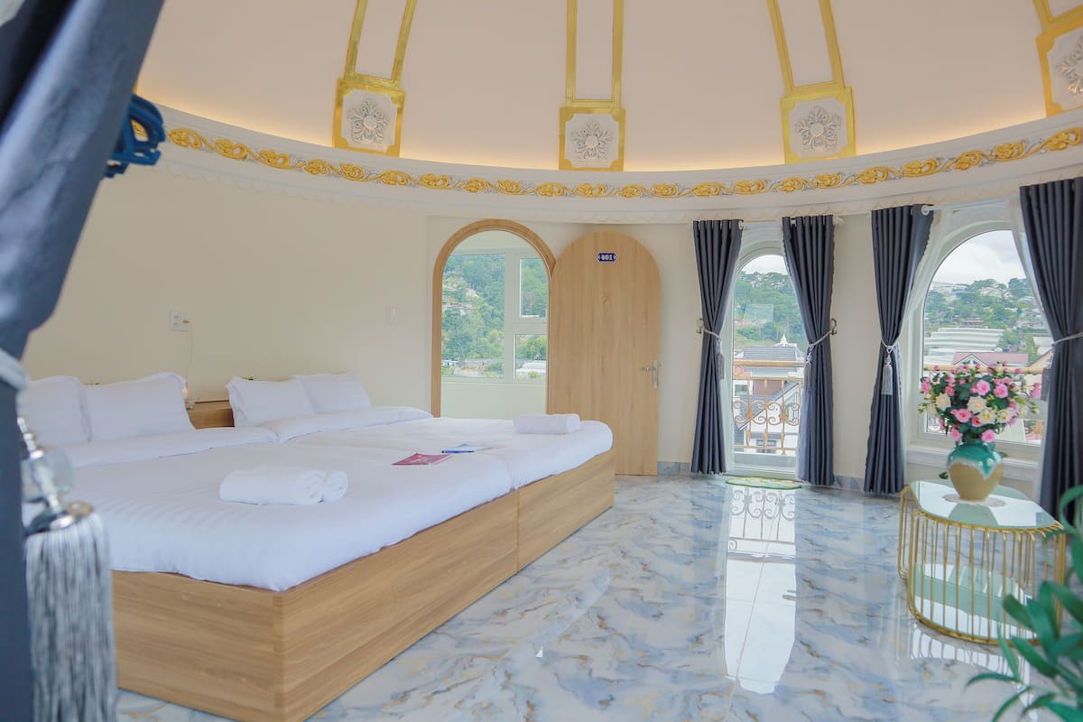 Un dormitorio amplio con una cama grande, un balcón con cortinas y vistas a zonas verdes.