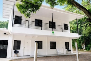 A two-story building with a balcony, white walls, and black shutters.