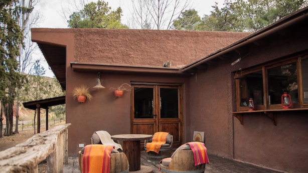 A rustic outdoor seating area with wooden barrels and a wooden table, surrounded by a wooden deck and a building with a brown exterior. - San Ignacio Estancia Andina (Guaymallen)