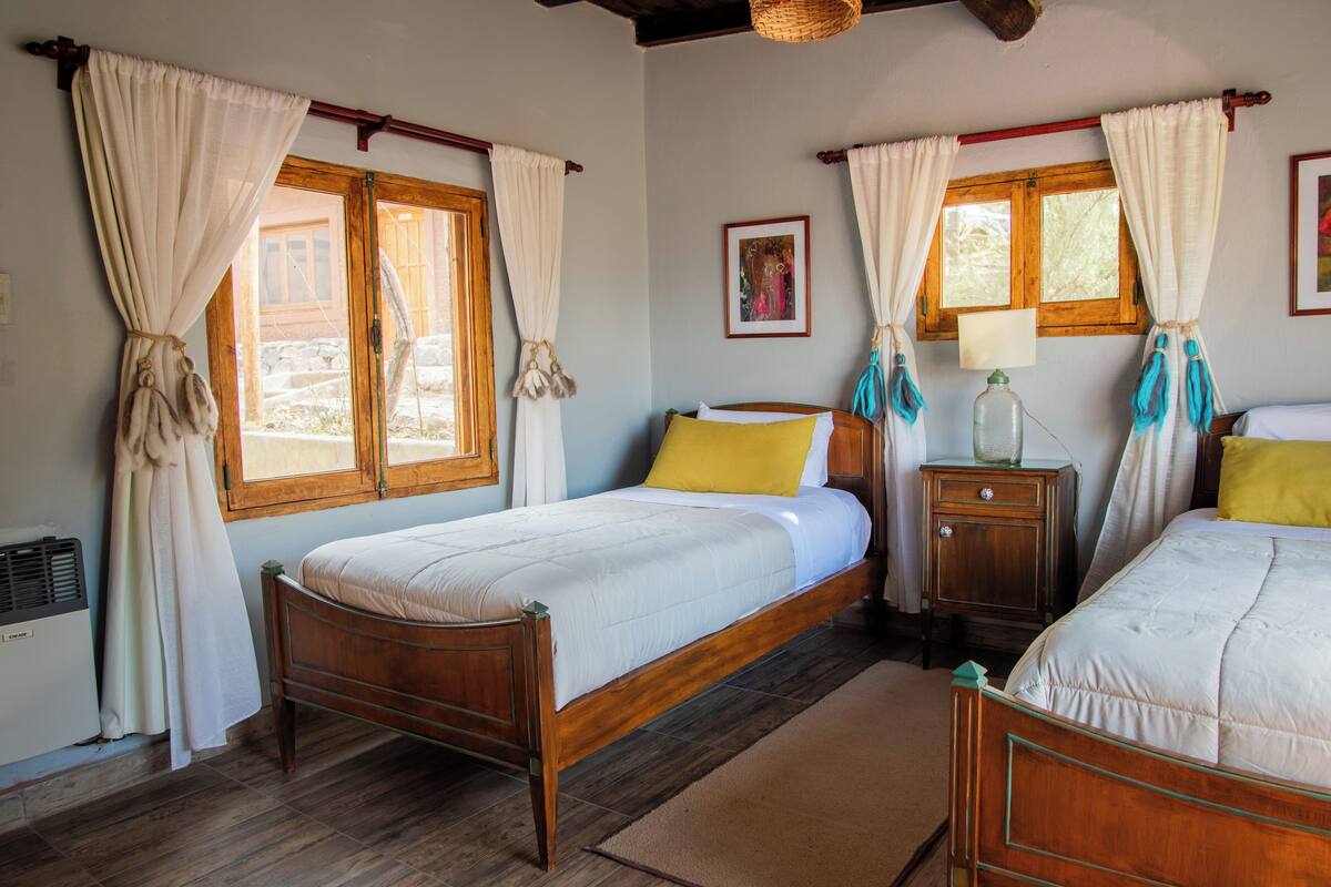 A bedroom with two wooden beds, a nightstand, a lamp, and a window with curtains.