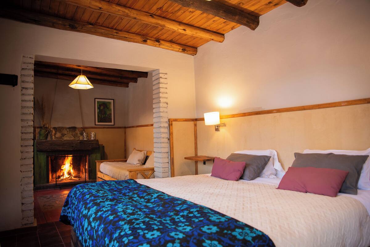 A cozy room with a fireplace, a bed with multiple pillows, and a wooden ceiling.