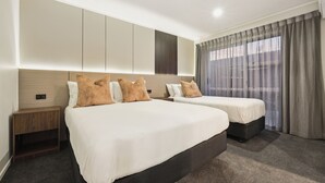 A hotel room with two beds, a wooden headboard, a small wooden nightstand, and a large window with curtains. - Aroha Motel (Auckland)