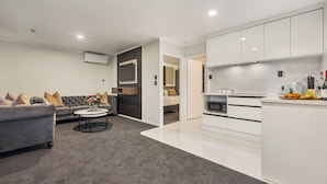 A modern living room with a grey sofa, a coffee table, and a kitchen area with white cabinets and appliances. - Aroha Motel (Auckland)