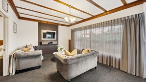 A modern living room with two grey sofas, a wooden ceiling, a flat-screen TV, and a large window with curtains. - Aroha Motel (Auckland)