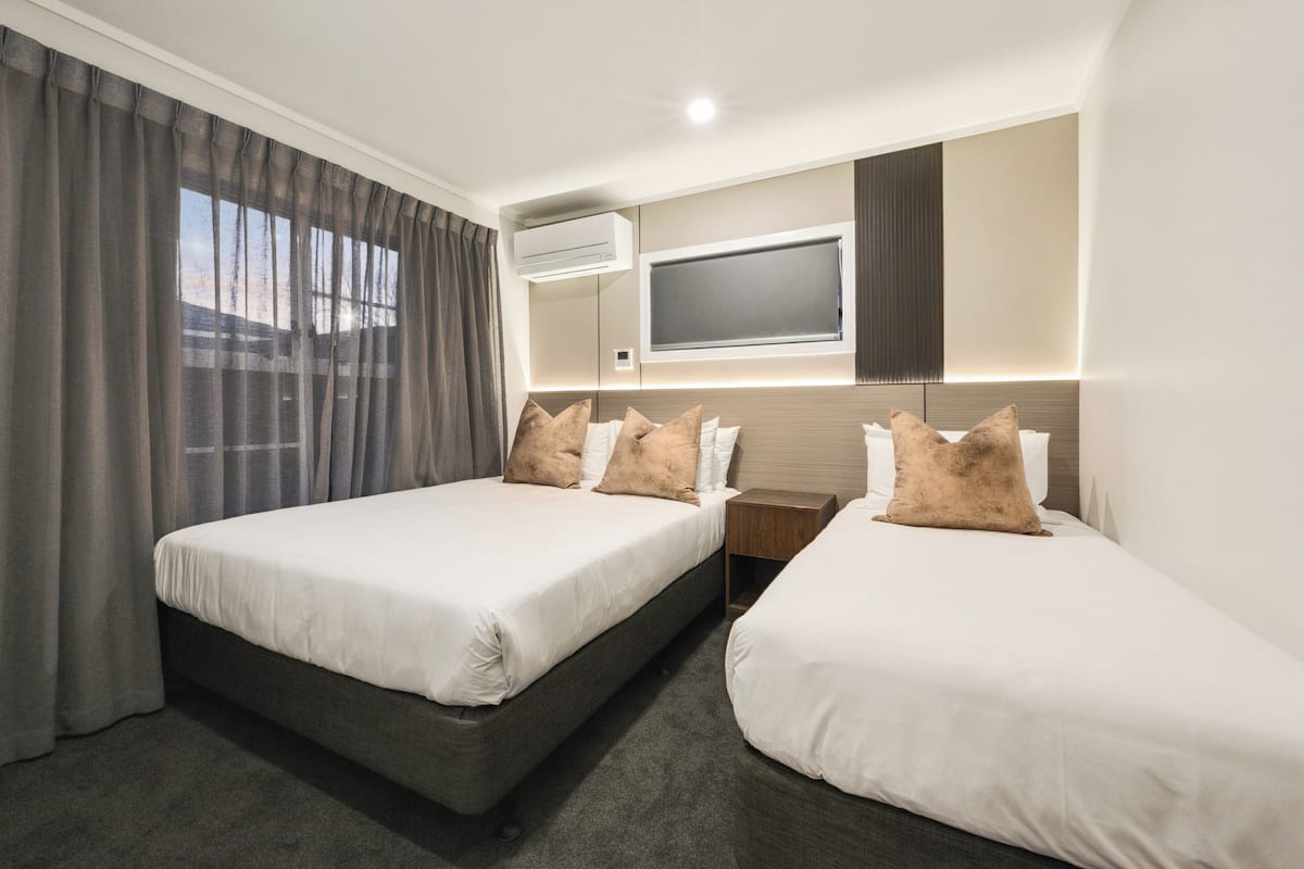 A hotel room with two beds, a flat-screen TV mounted on the wall, and an air conditioning unit.