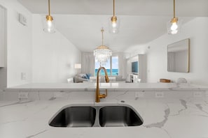 Eine moderne Küche mit einer Spüle, Marmorarbeitsplatten und Pendelleuchten.