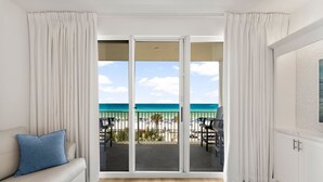 Una habitación con sofá, alfombra estampada, chimenea y balcón con vista a la playa y al océano.