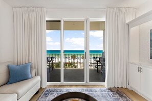 Una habitación con sofá, alfombra estampada, chimenea y balcón con vista a la playa y al océano.