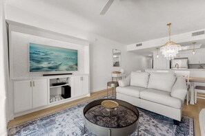 Una sala de estar moderna con televisor de pantalla plana, sofá blanco, mesa de centro redonda y una araña.