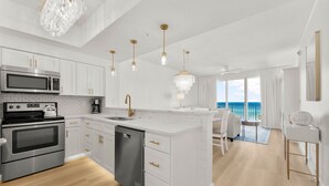 Una cocina moderna con armarios blancos, electrodomésticos de acero inoxidable y vista al océano.