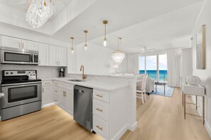 Una cocina moderna con armarios blancos, electrodomésticos de acero inoxidable y vista al océano.