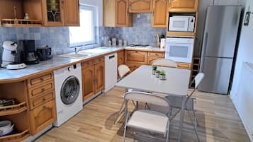 A modern kitchen with wooden cabinets, a stainless steel refrigerator, a microwave, and a washing machine.