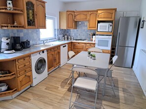 A modern kitchen with wooden cabinets, a stainless steel refrigerator, a microwave, and a washing machine. - Holiday Home in Telgruc-sur-mer by Sandy Beach (Telgruc-sur-Mer)